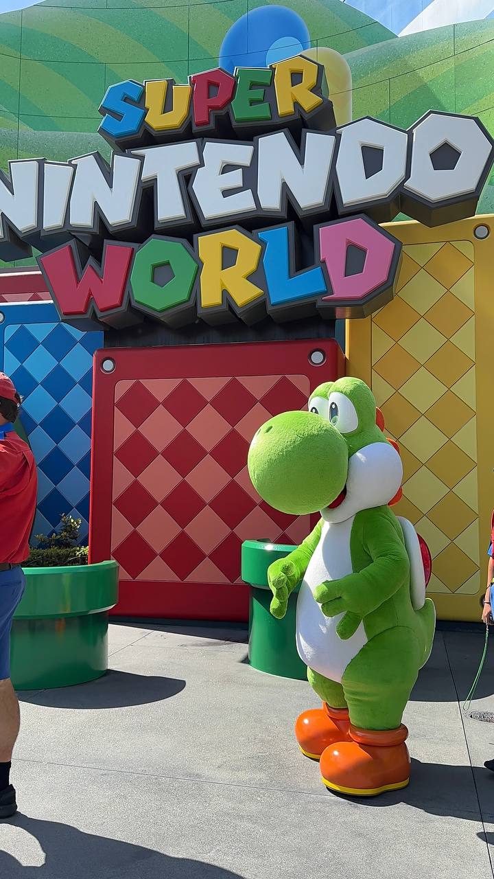 Yoshi posing in front of the Super Nintendo World sign