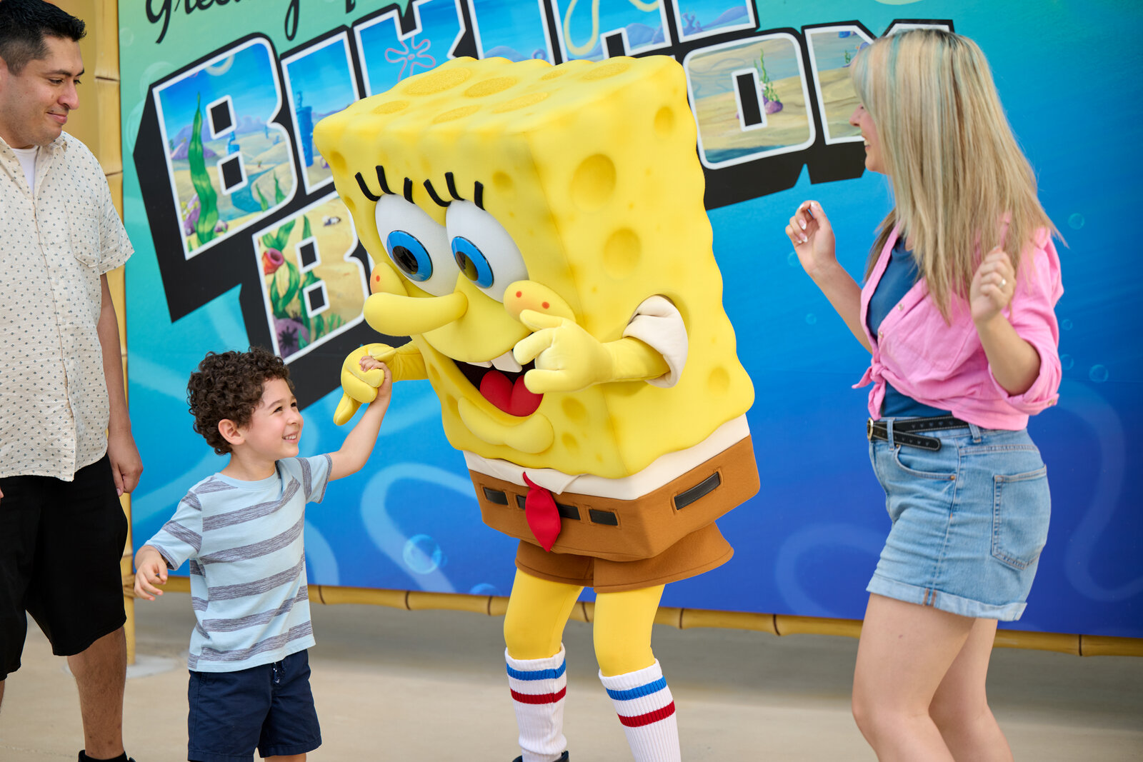 SpongeBob greets a family in front of a Bikini Bottom backdrop at Universal Kids Resort
