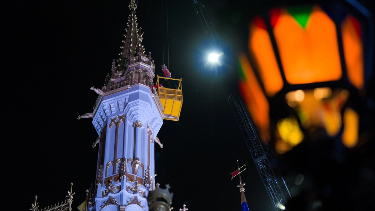 Crews painting a Cinderella Castle spire at night from a crane lift