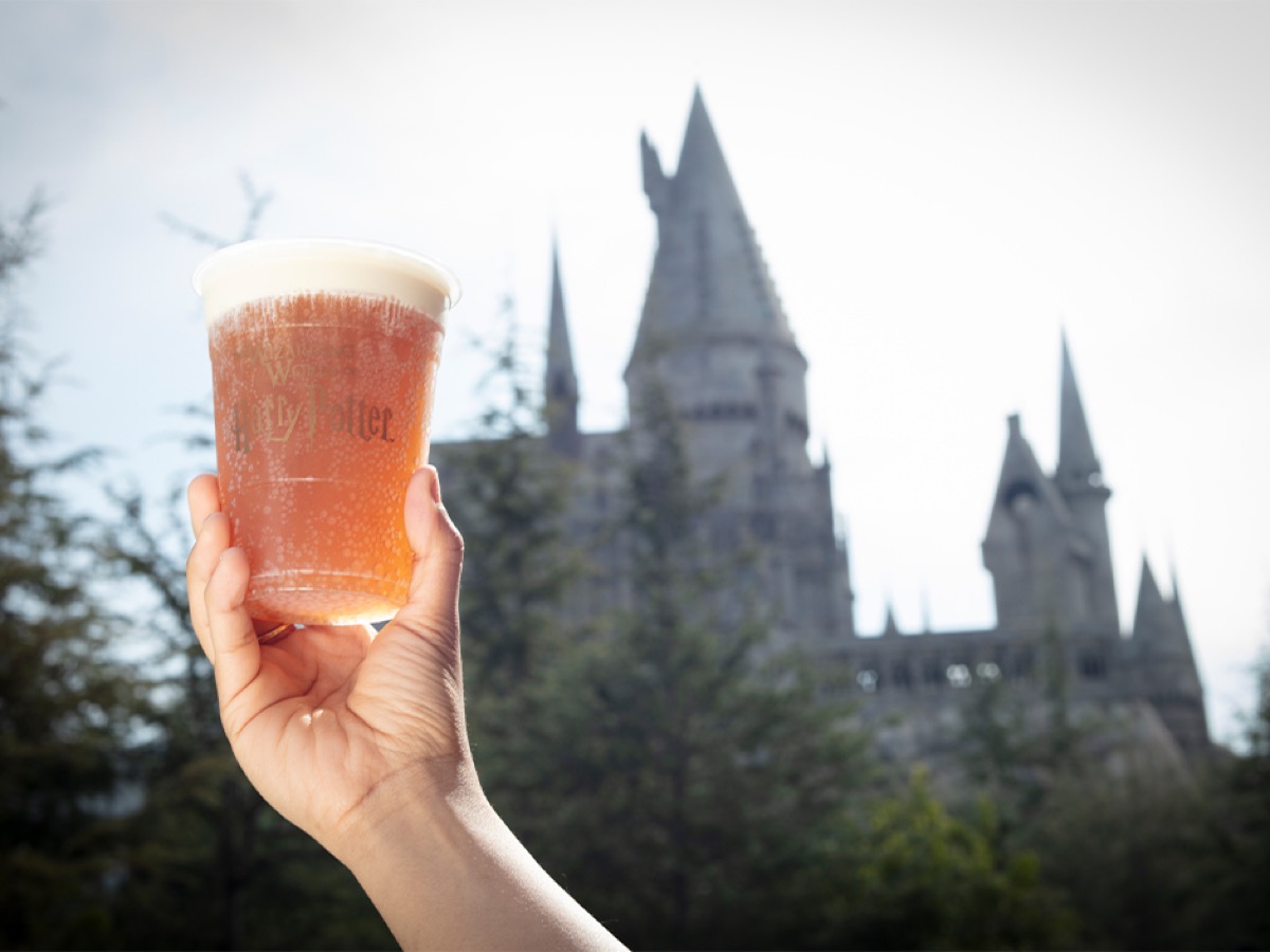 A cup of Butterbeer held up in front of Hogwarts castle at Universal Studios Hollywood