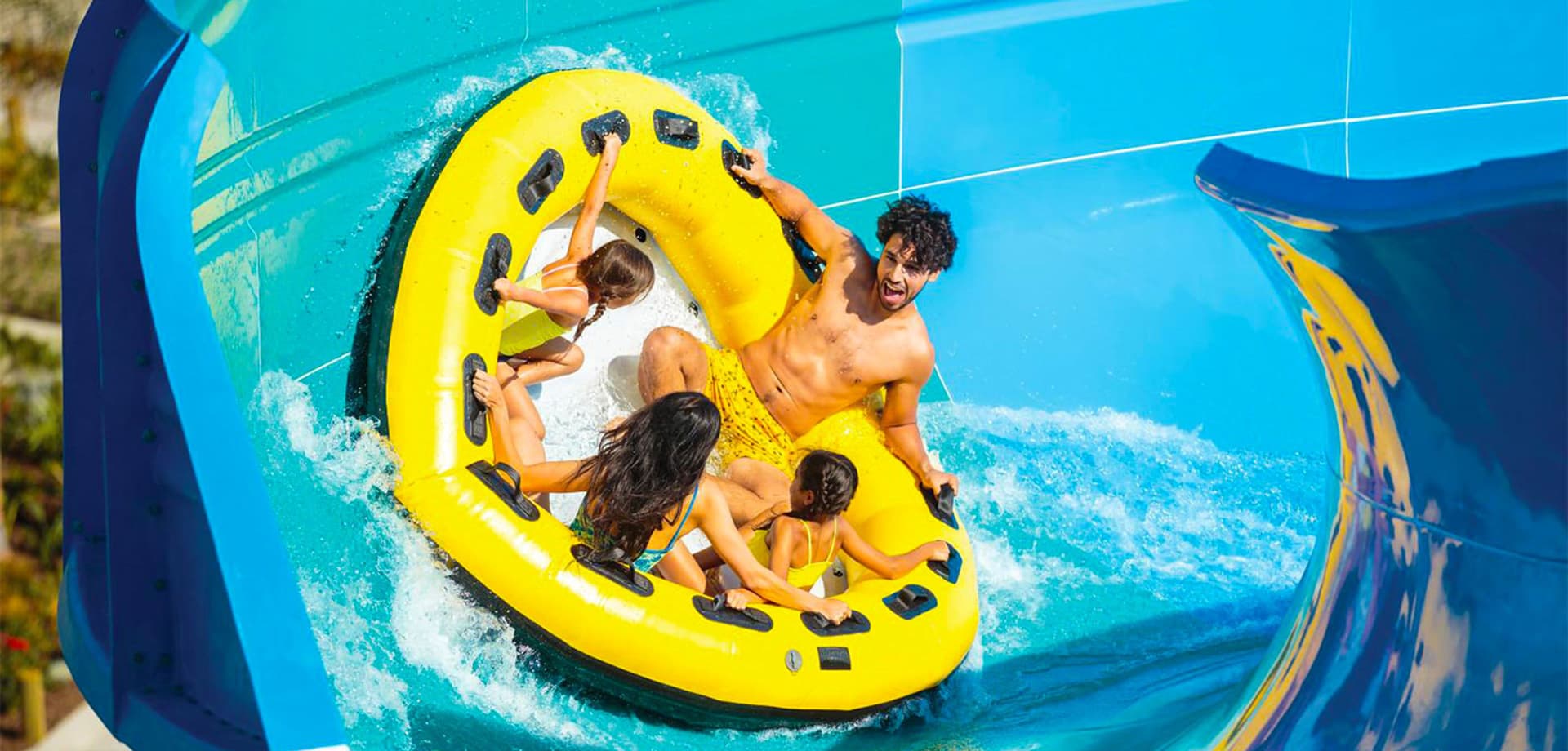 Four riders in a yellow family raft climb a banked wall on a water slide at Knott's Soak City
