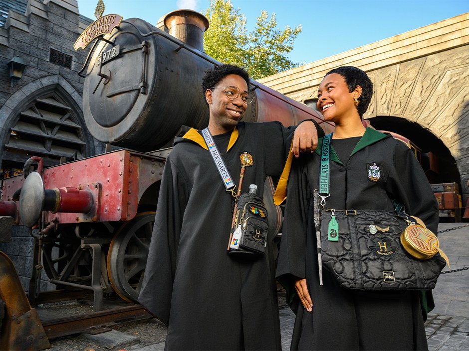 Two guests in Hogwarts house robes carrying Lug Build-A-Bag bags beside the Hogwarts Express