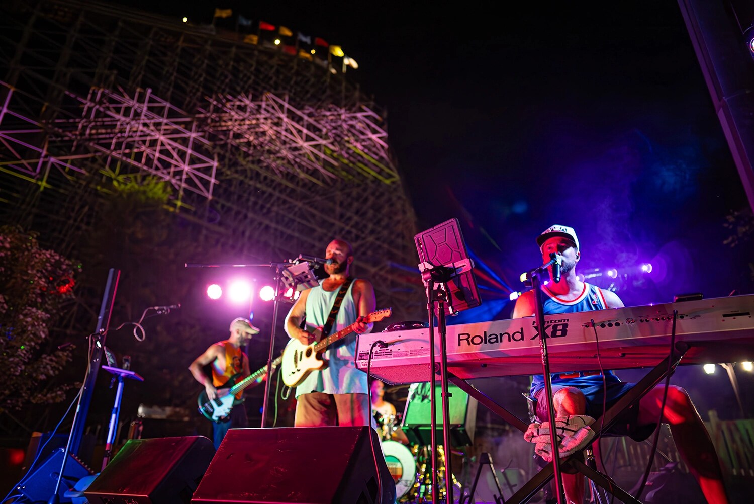 A band plays on a lit stage at night in front of a wooden roller coaster during Friday Night Live at Holiday World