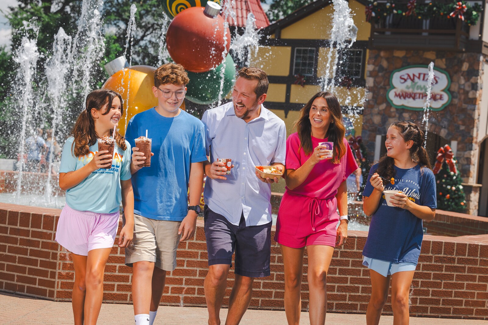 A family walks with food and drinks past the fountain at Santas Merry Marketplace in Holiday World