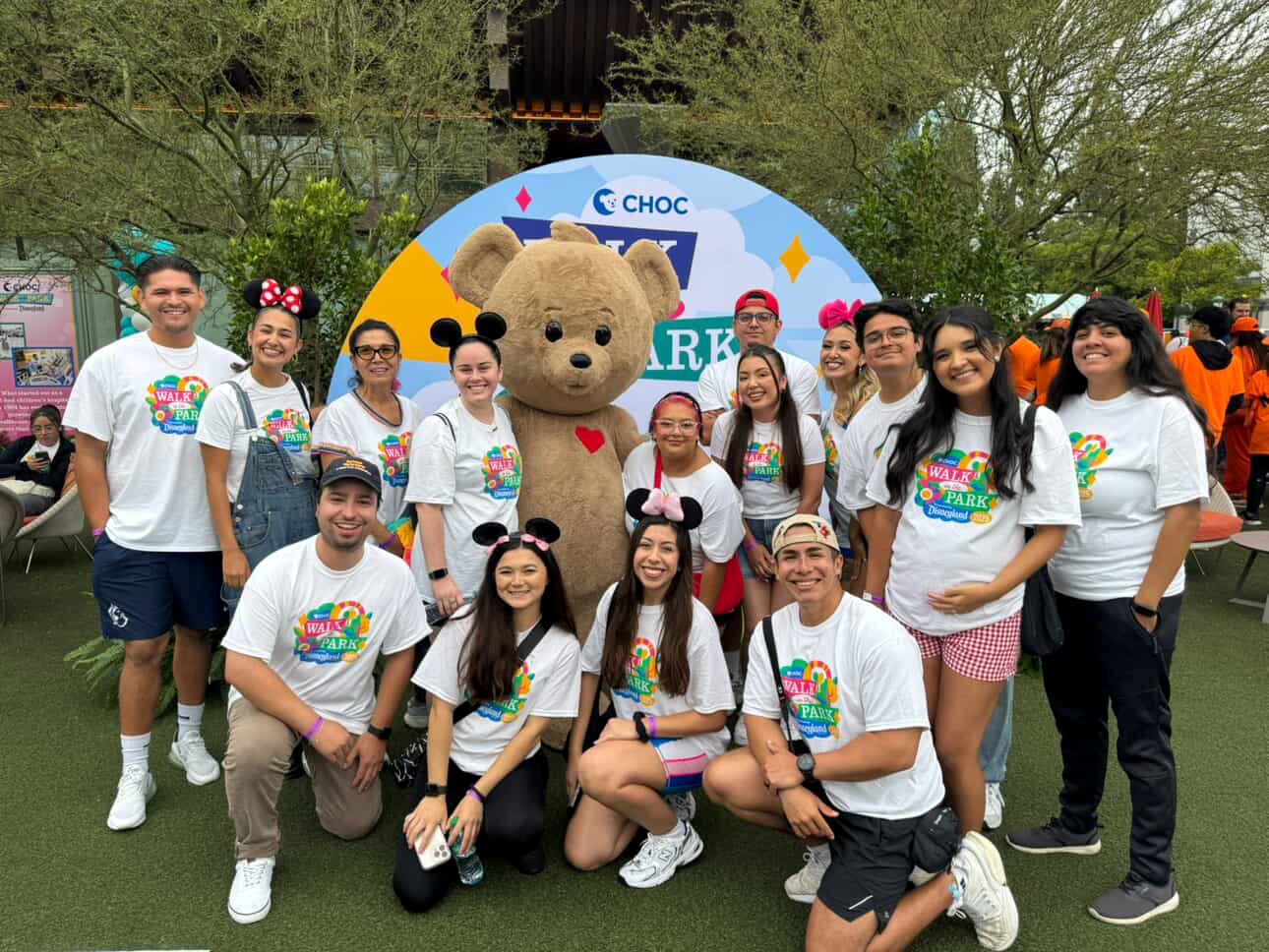 CHOC Walk participants posing with the CHOC bear mascot in front of a Walk in the Park backdrop
