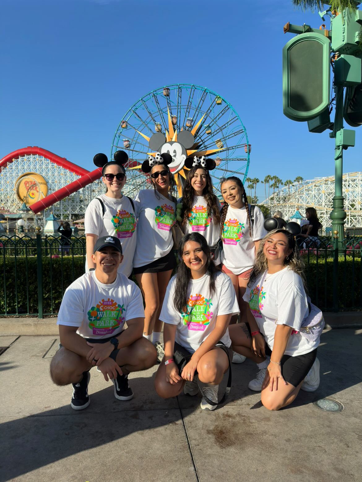 Seven walkers in CHOC Walk in the Park shirts posing in front of Pixar Pier at Disney California Adventure