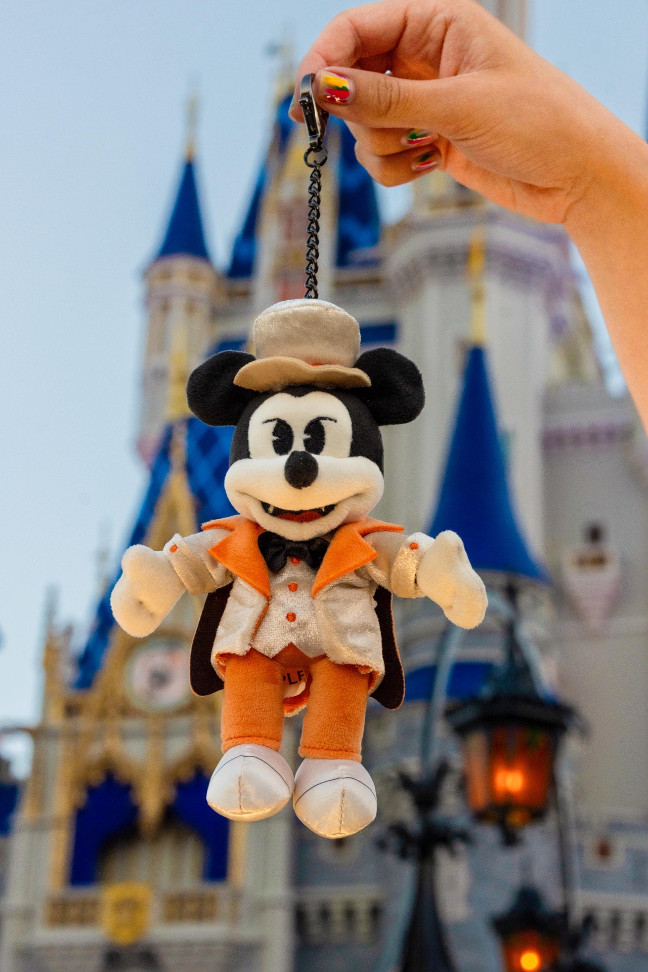 Mickey Mouse Vampire plush keychain held in front of Cinderella Castle