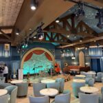 Blue lounge chairs, round tables and an arched stage inside Hurly-Burly at Disney’s BoardWalk.