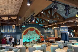 Blue lounge chairs, round tables and an arched stage inside Hurly-Burly at Disney’s BoardWalk.