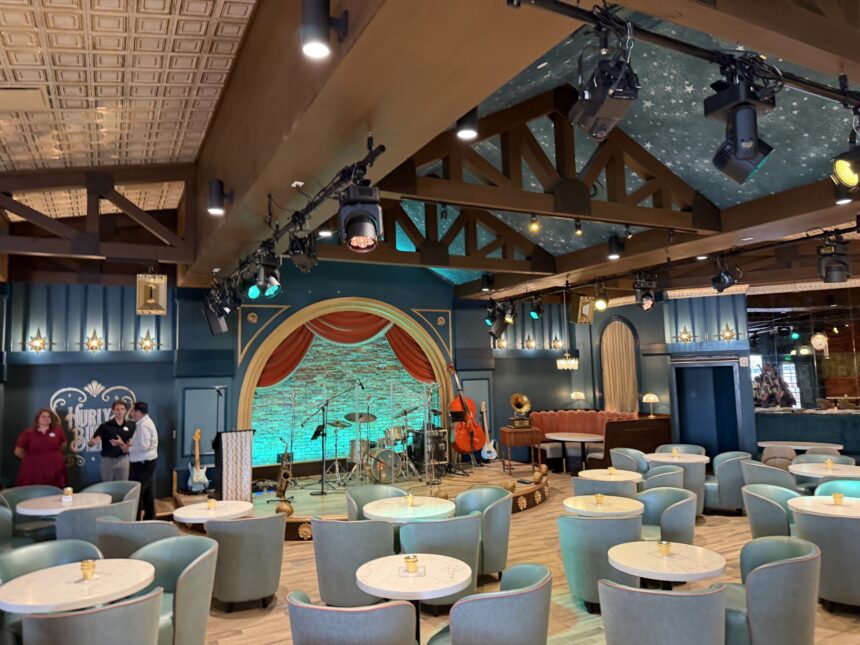 Blue lounge chairs, round tables and an arched stage inside Hurly-Burly at Disney’s BoardWalk.