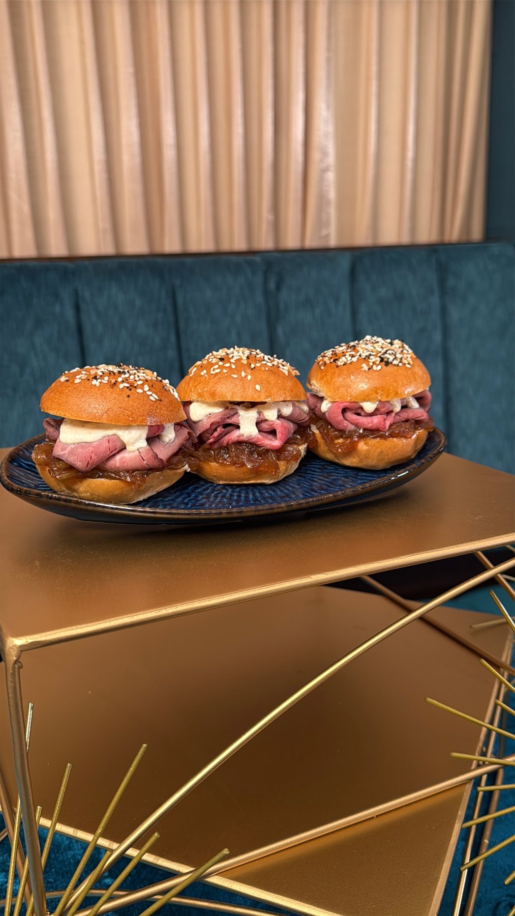 Three roast beef sliders on seeded buns, arranged on a dark plate.