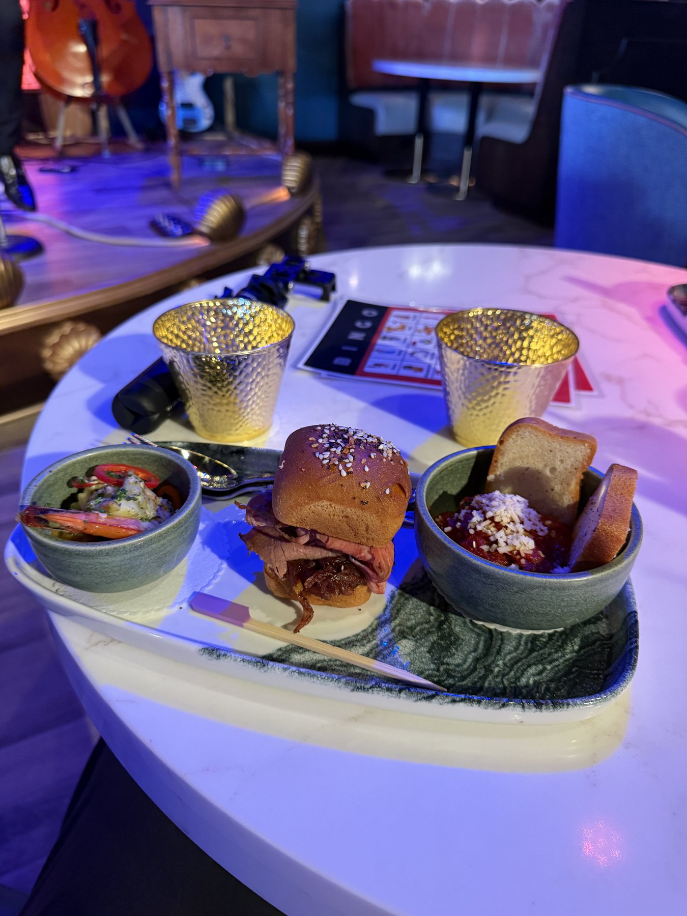 A preview plate with a roast beef slider, bread and small bowls on a lounge table.