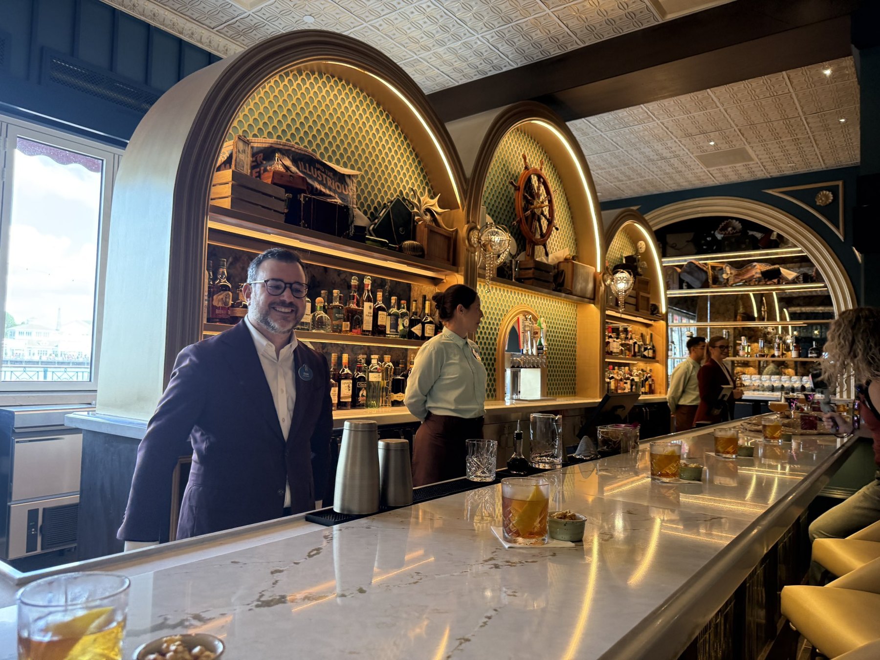The bar at Hurly-Burly, with illuminated arched shelves, a pale countertop and blue cabinetry.